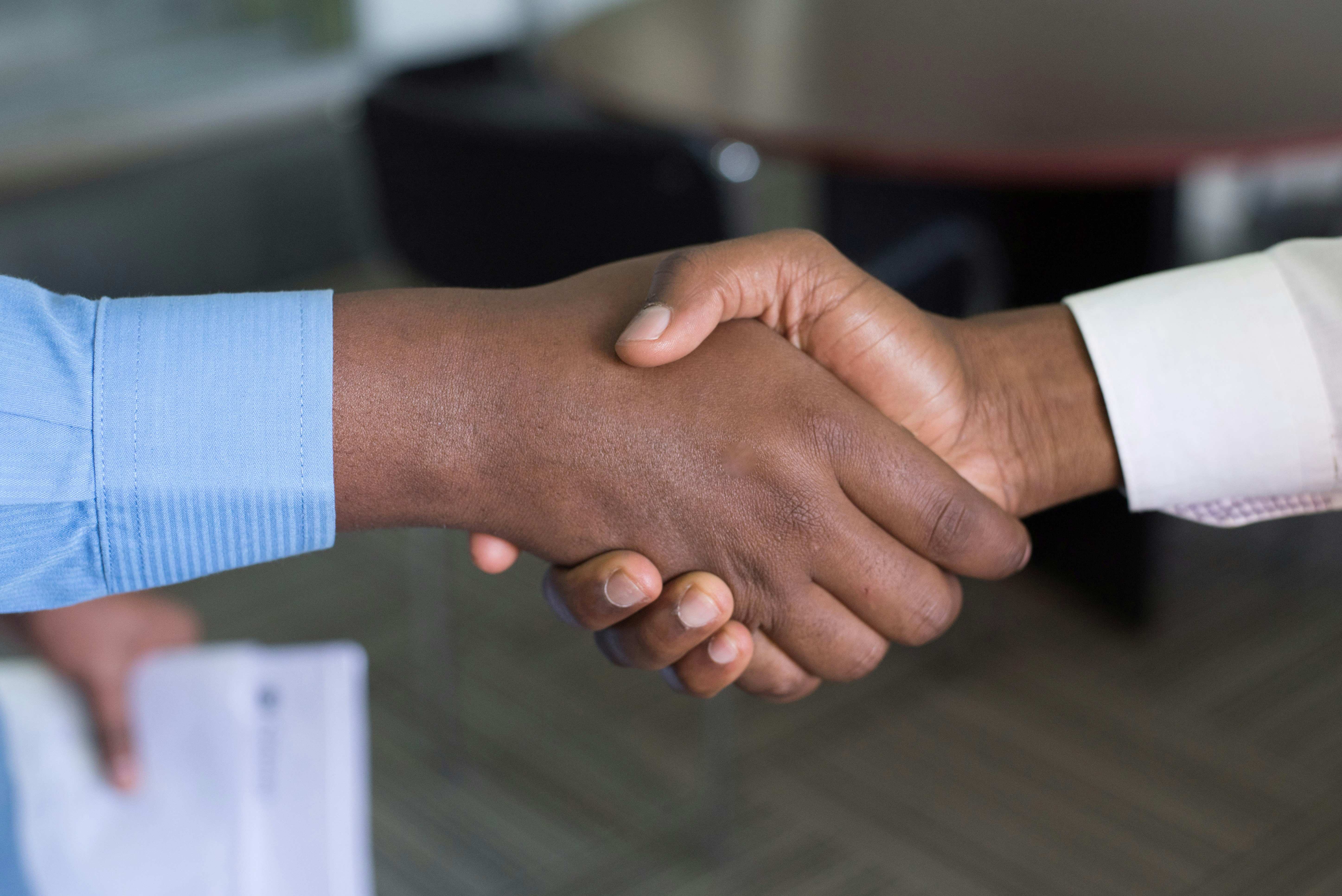 Two hands clasped in a firm business handshake within an office setting, symbolizing the strong trust, successful partnership, and relation-building crucial for achieving high customer retention rates and client loyalty.